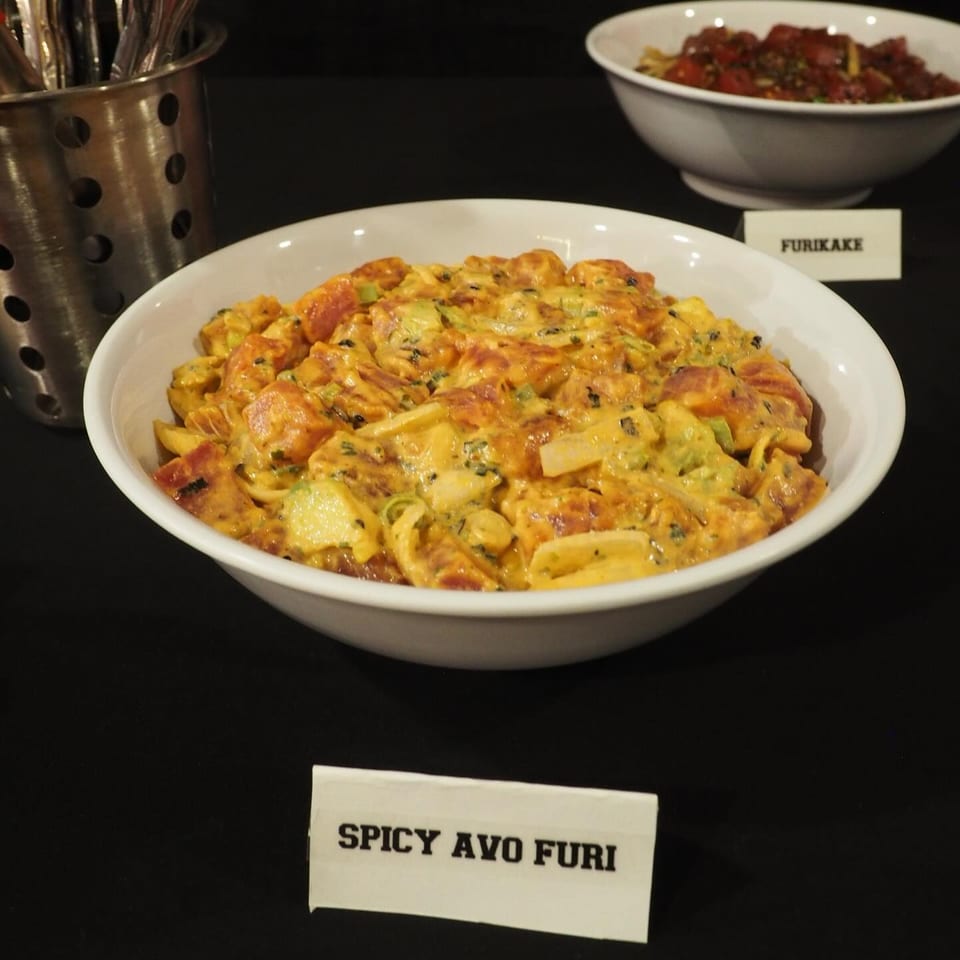 Bowl of creamy spicy ayo furi pasta with vegetables and herbs displayed on a buffet table.