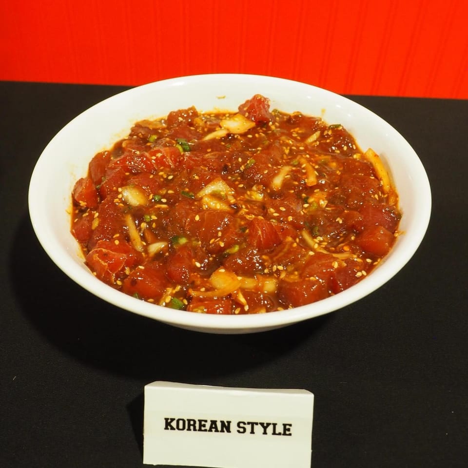 Bowl of Korean-style raw tuna chunks in a spicy red sauce, garnished with sesame seeds, garlic, and green onions.